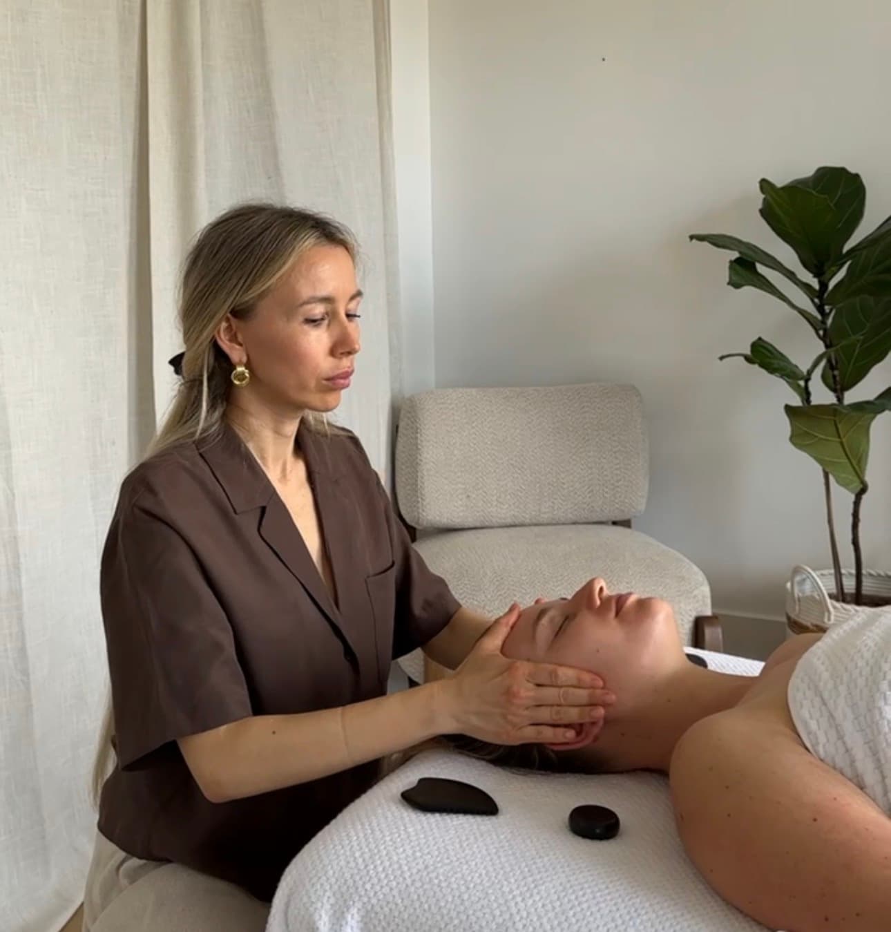 A practitioner performs a facial massage on a client in a serene, minimalist spa setting.